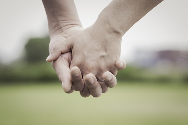 Hands of bride and groom holding each other's hand in the green field