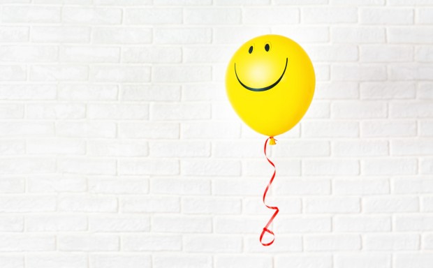 Yellow ballon with smile hangs aganst white wall