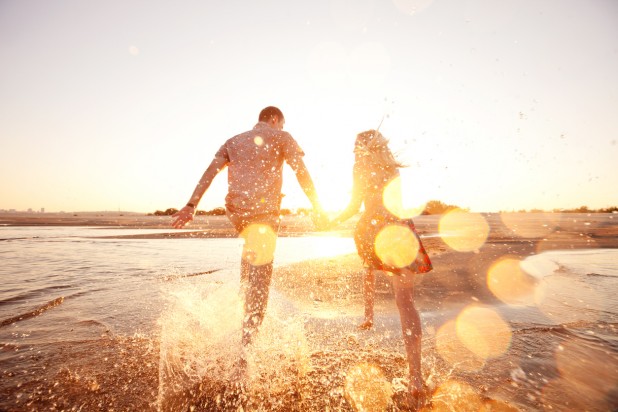 A happy couple runs through waves on sunlit beach