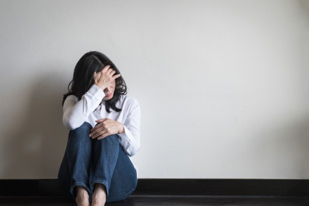 Stressful woman sitting sadly with emotional depression and anxiety on the floor in home living room with white wall