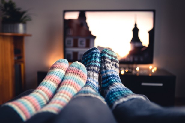 Couple with socks and woolen stockings watching movies or series on tv in winter. Woman and man sitting or lying together on sofa couch in home living room using online streaming service.