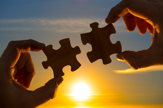 two hands connect the puzzle details, against the sky of the sun.