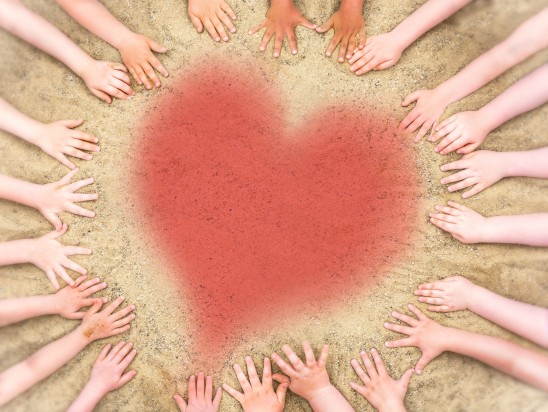 Children's hands in the sand with a heart in their middle