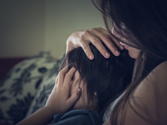 Closeup sad little boy being hugged by his mother at home. Parenthood, Love and togetherness concept.