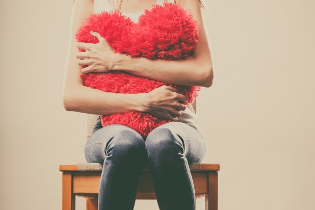 Sad unhappy woman holding red heart pillow
