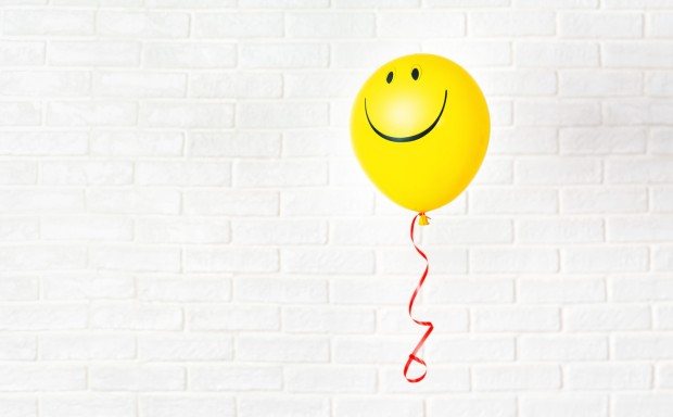 Yellow ballon with smile hangs aganst white wall